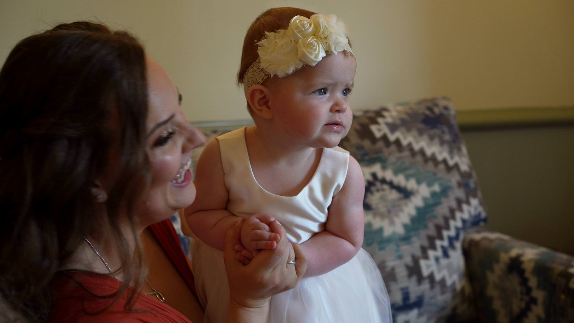 baby flower girls stands next to her Mum laughing