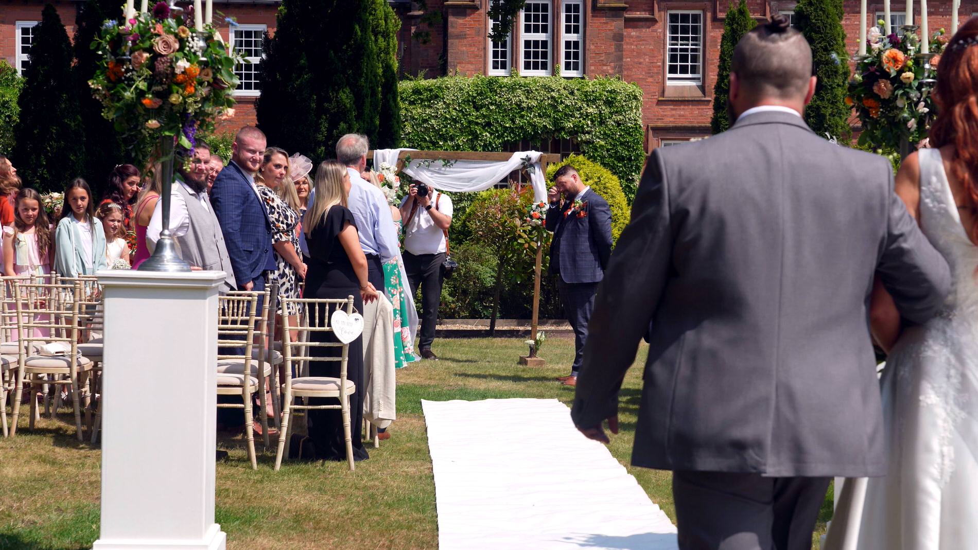 Bride walks down the aisle at outdoor garden ceremony at Nunsmere hall