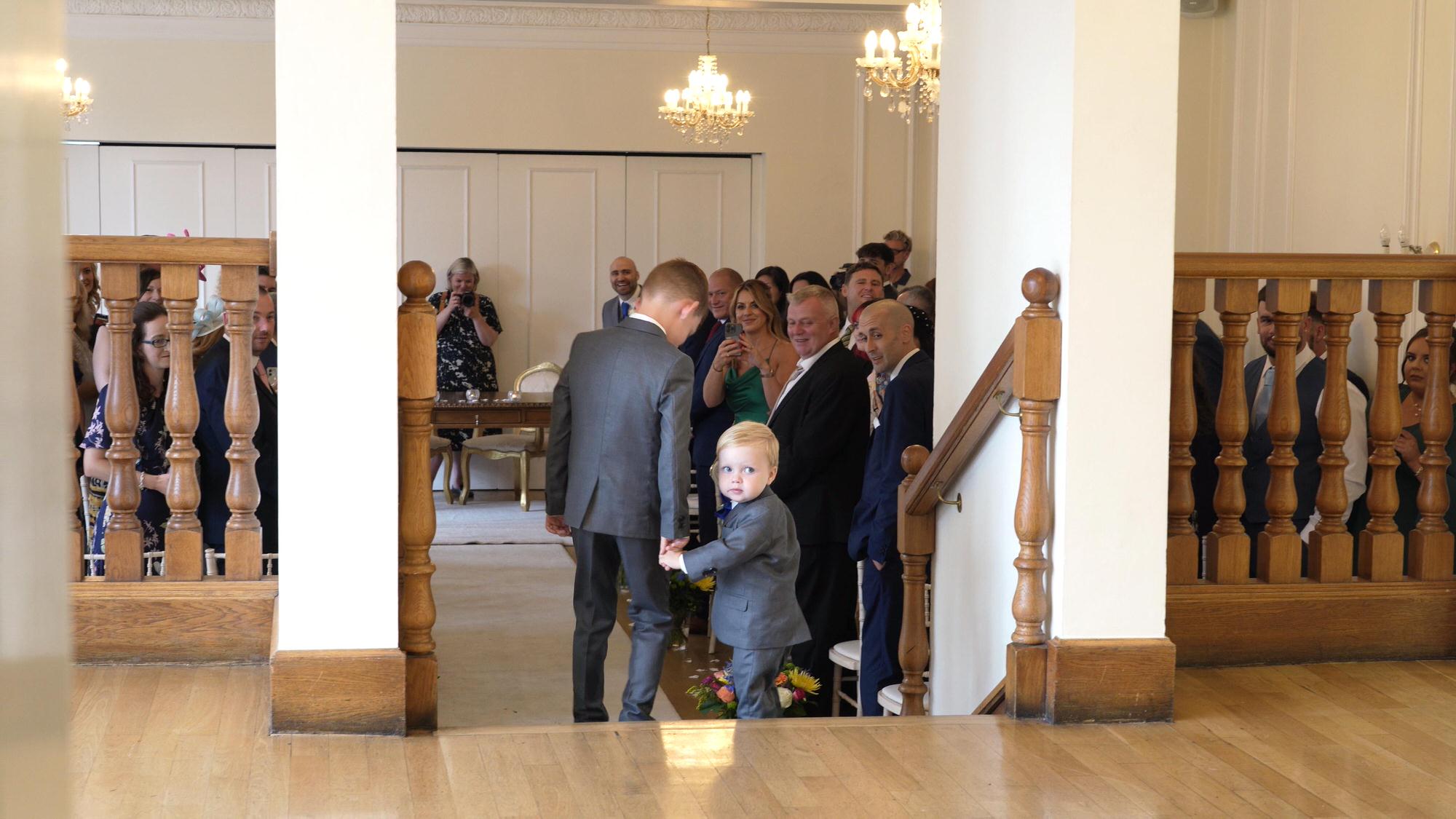 a little page boy looks back at his mum before walking down the aisle