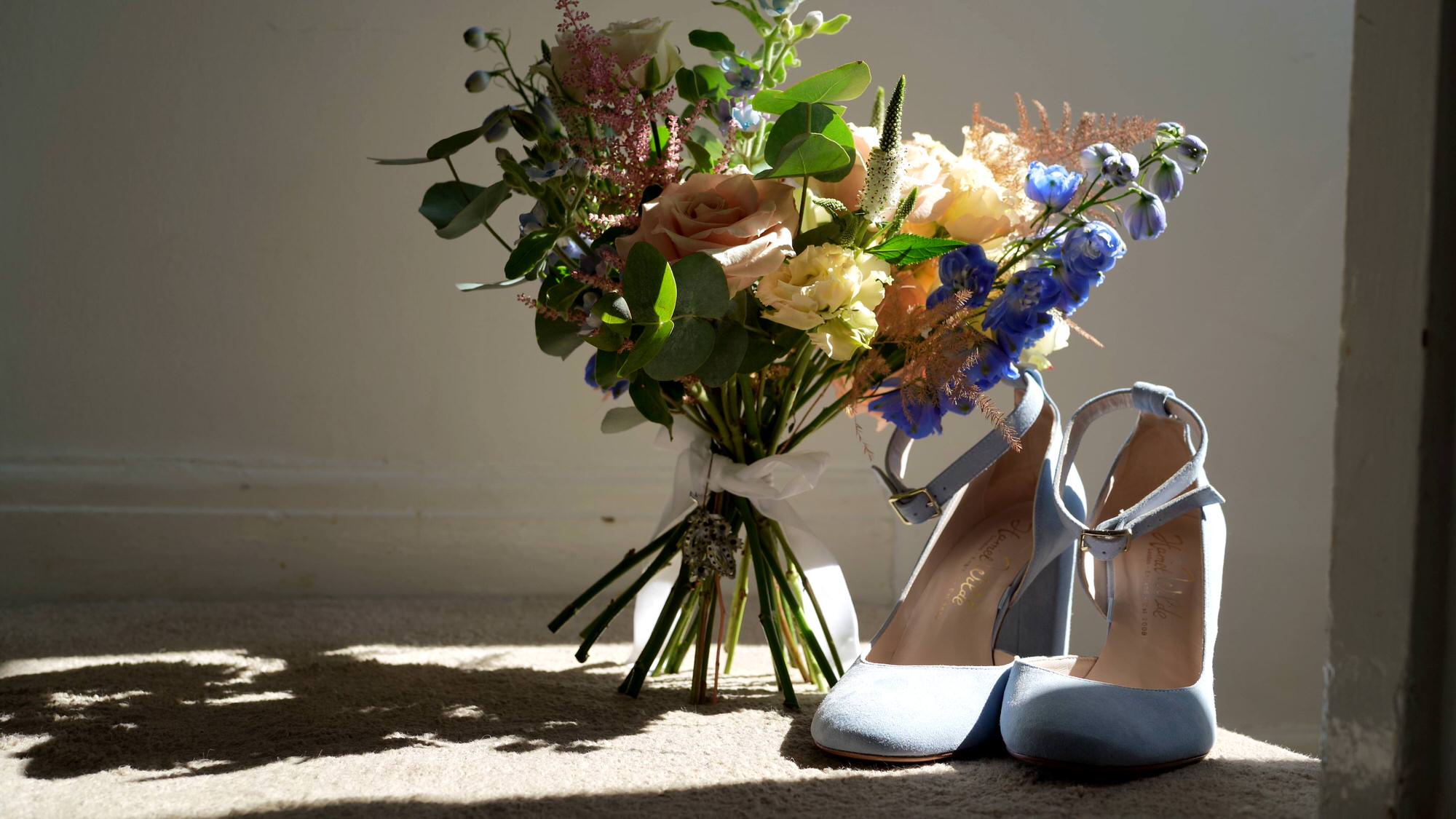 a hand tied colourful bridal bouquet sits by baby blue shoes
