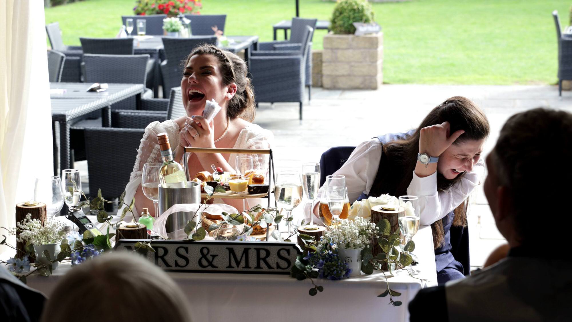 both brides laugh in embarrassment at a funny speech at The Aviary