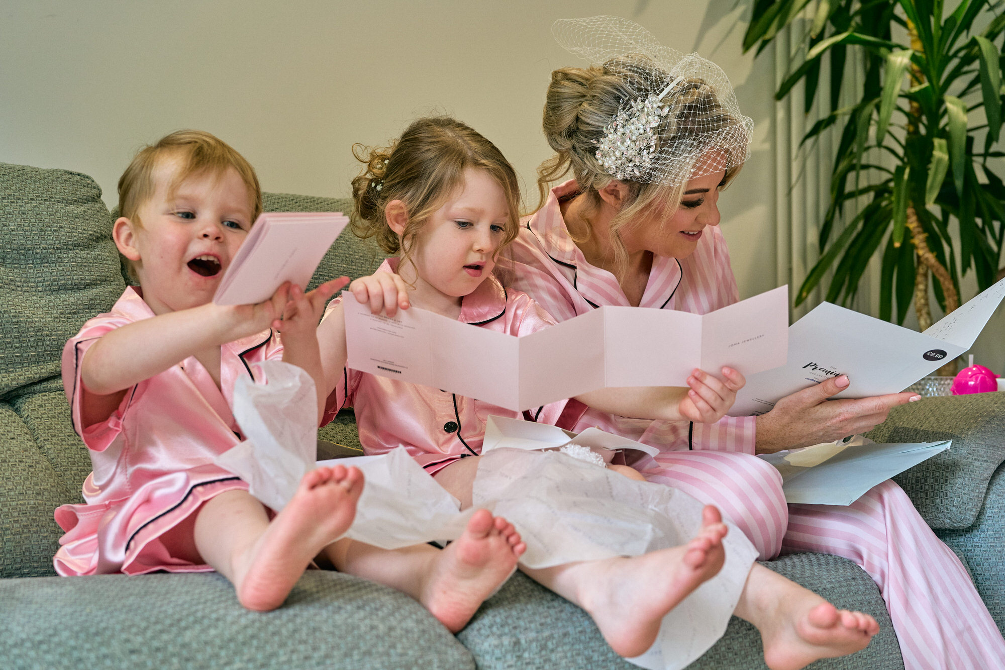 a bride sits with her young daughters reading wedding cards in their PJs
