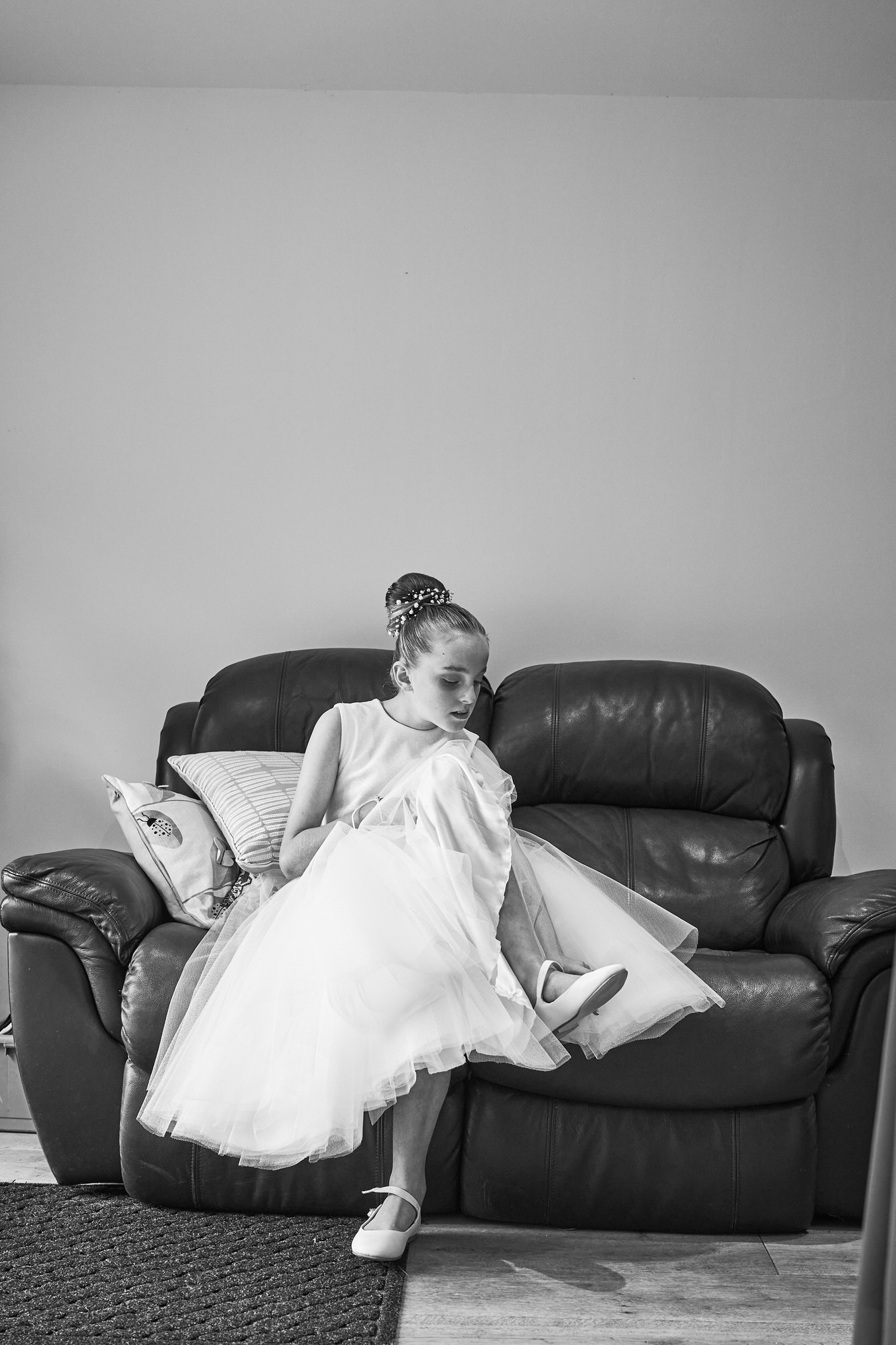 a natural portrait of a flower girl adjusting her wedding shoes sitting down