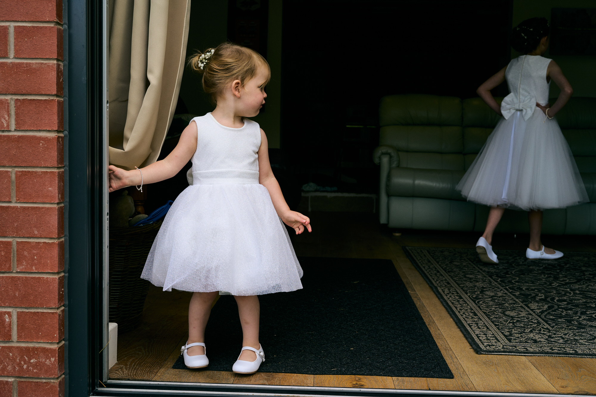 a little flowergirl stands in a doorway on the wedding morning in Birkdale
