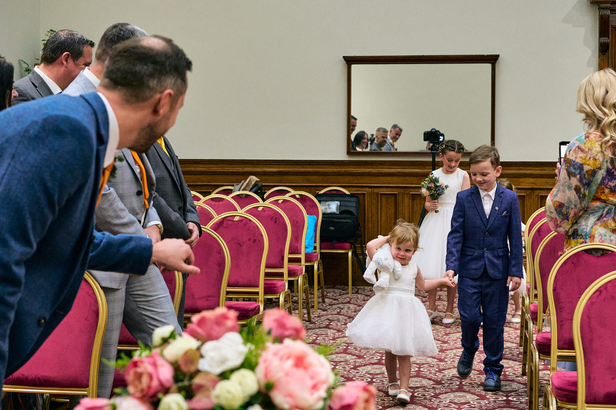the groom leans down to welcome the flower girl down the aisle