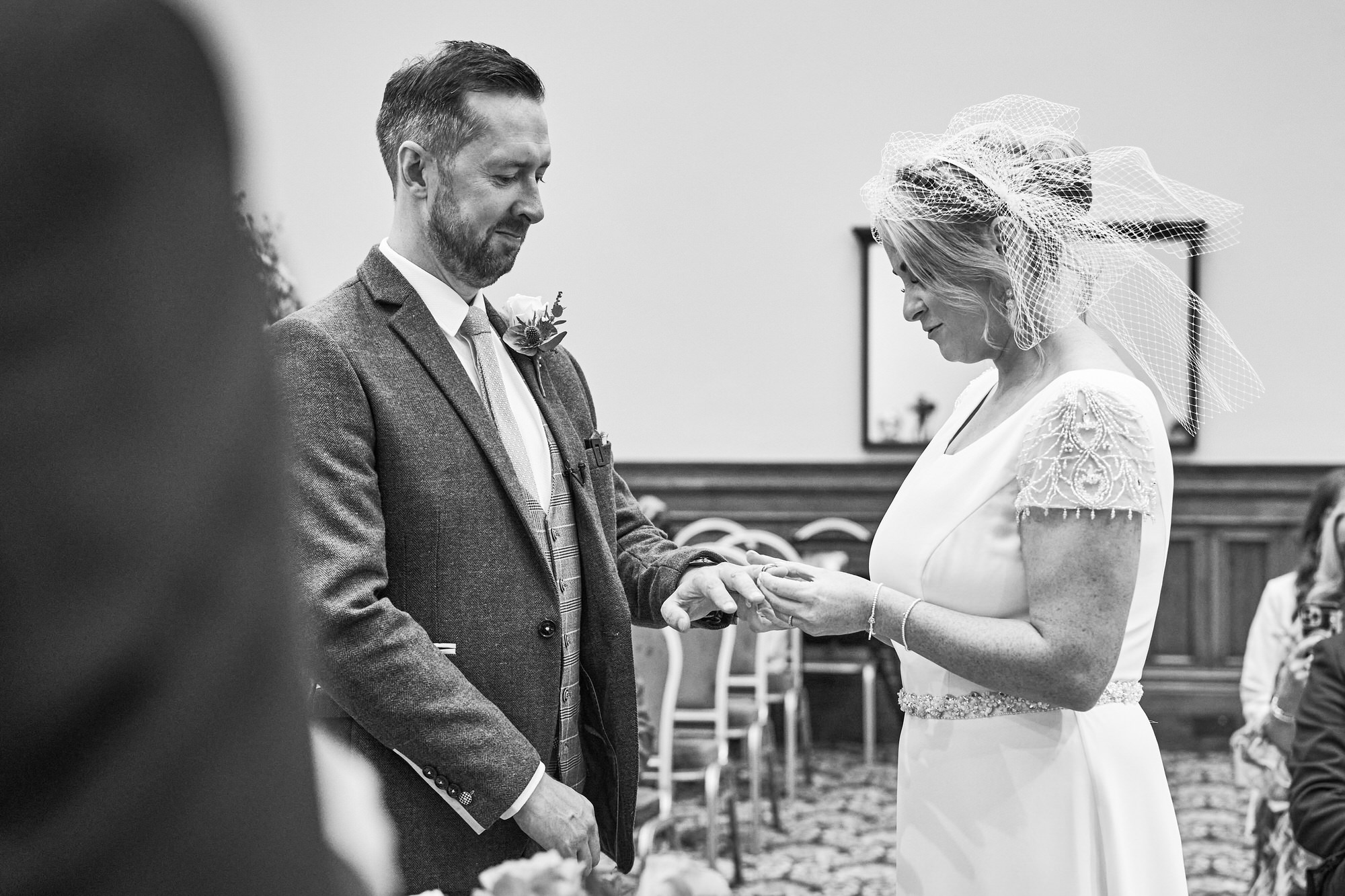 a black and white photo of the bride placing a wedding ring on the groom