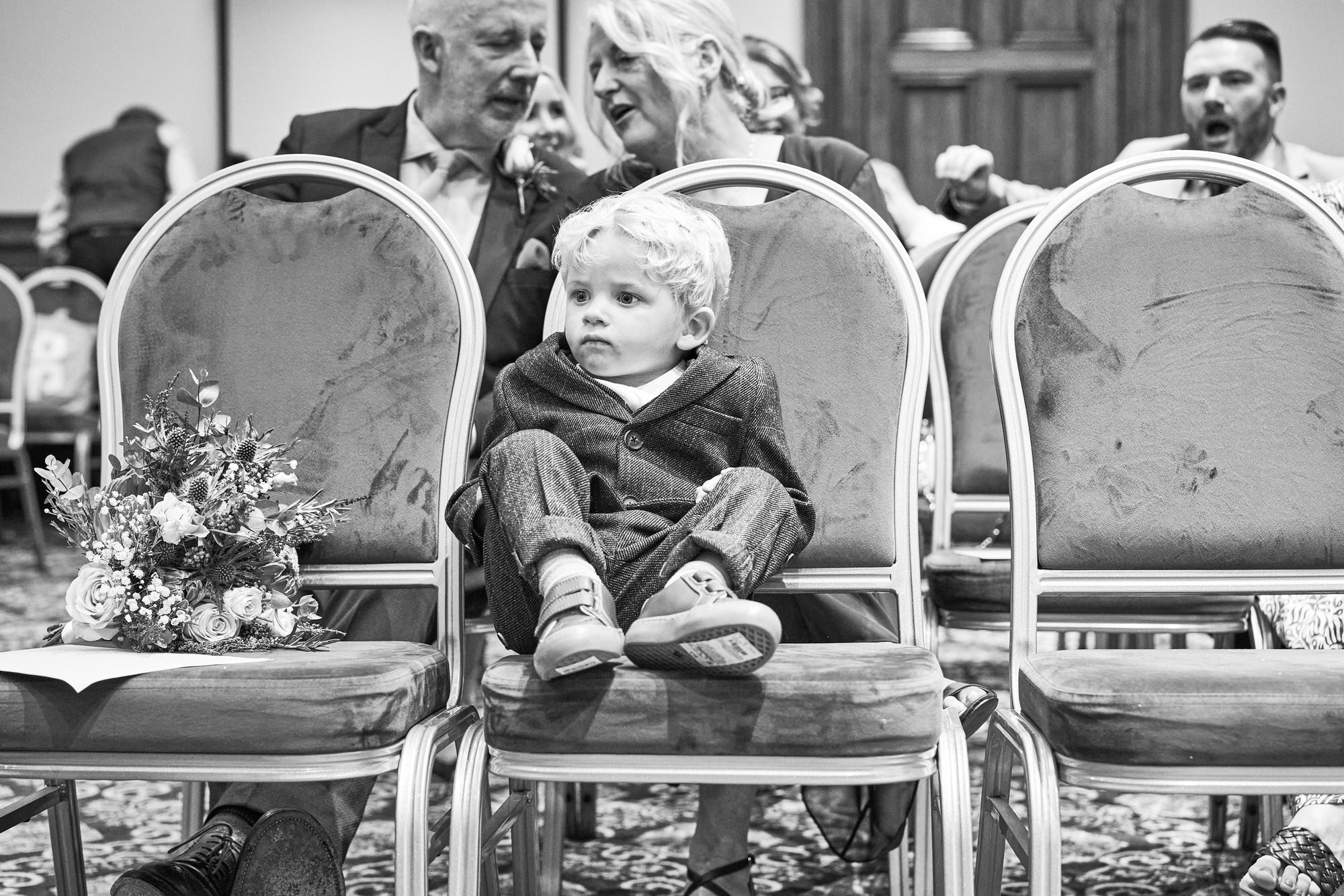 a little page boy sits alone on the front row during a wedding ceremony