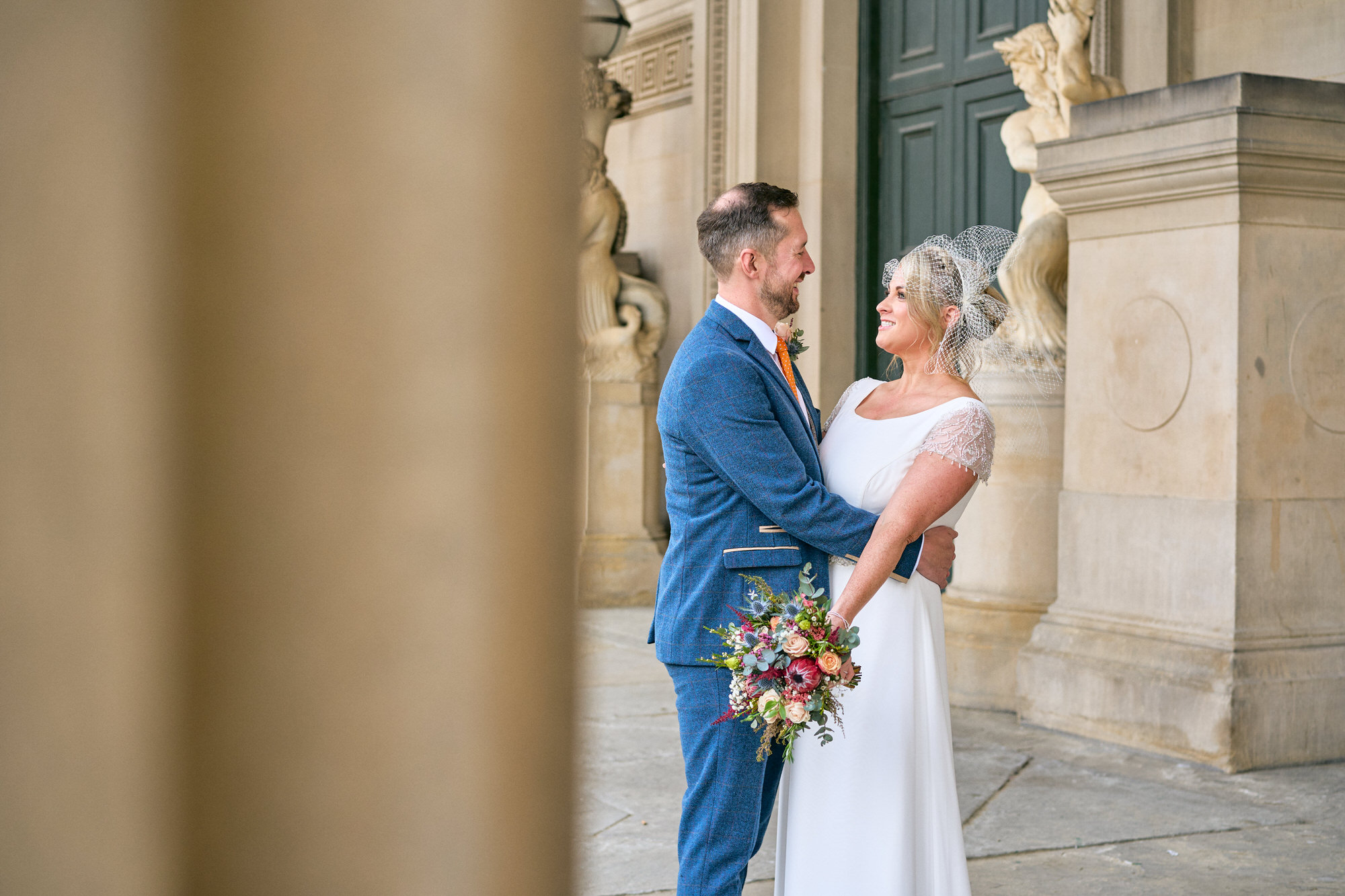 a wedding couple stand between the pillars at at St Georges Hall