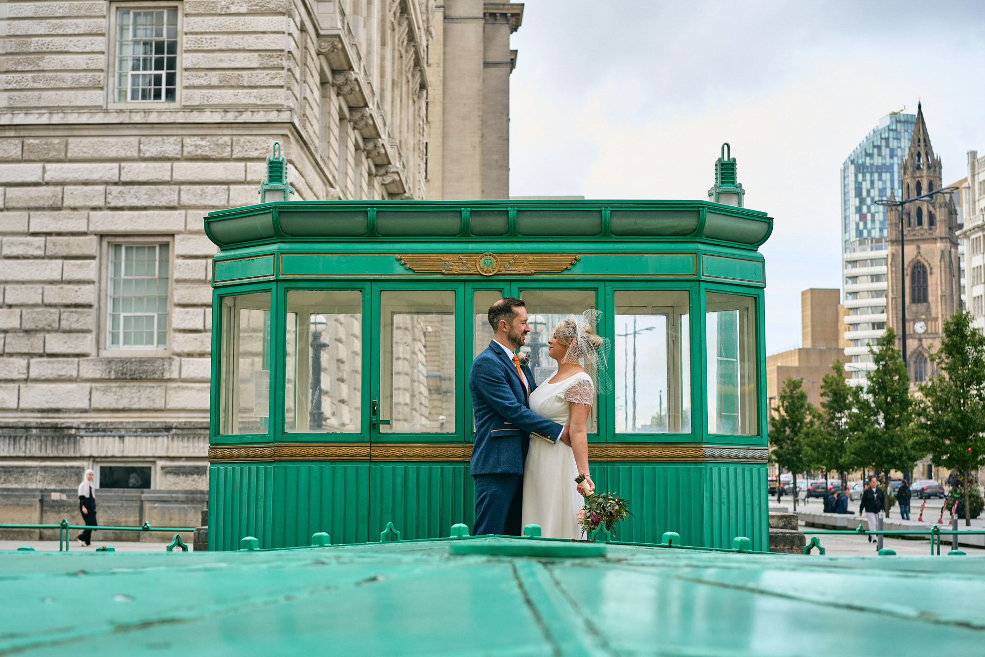 a couple chat in front of the restored mersey toll booth by the three graces