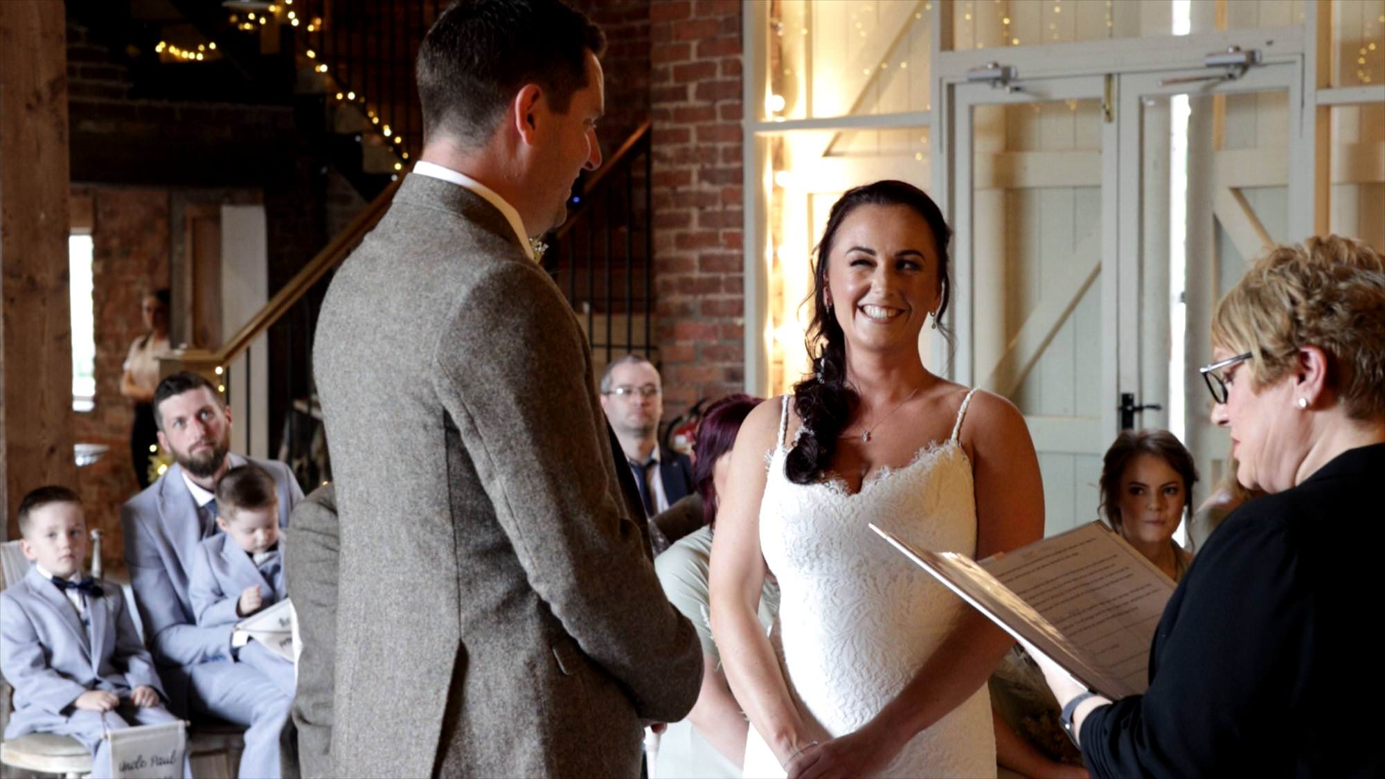 a bride has a cheeky wink at her groom during the barn wedding ceremony