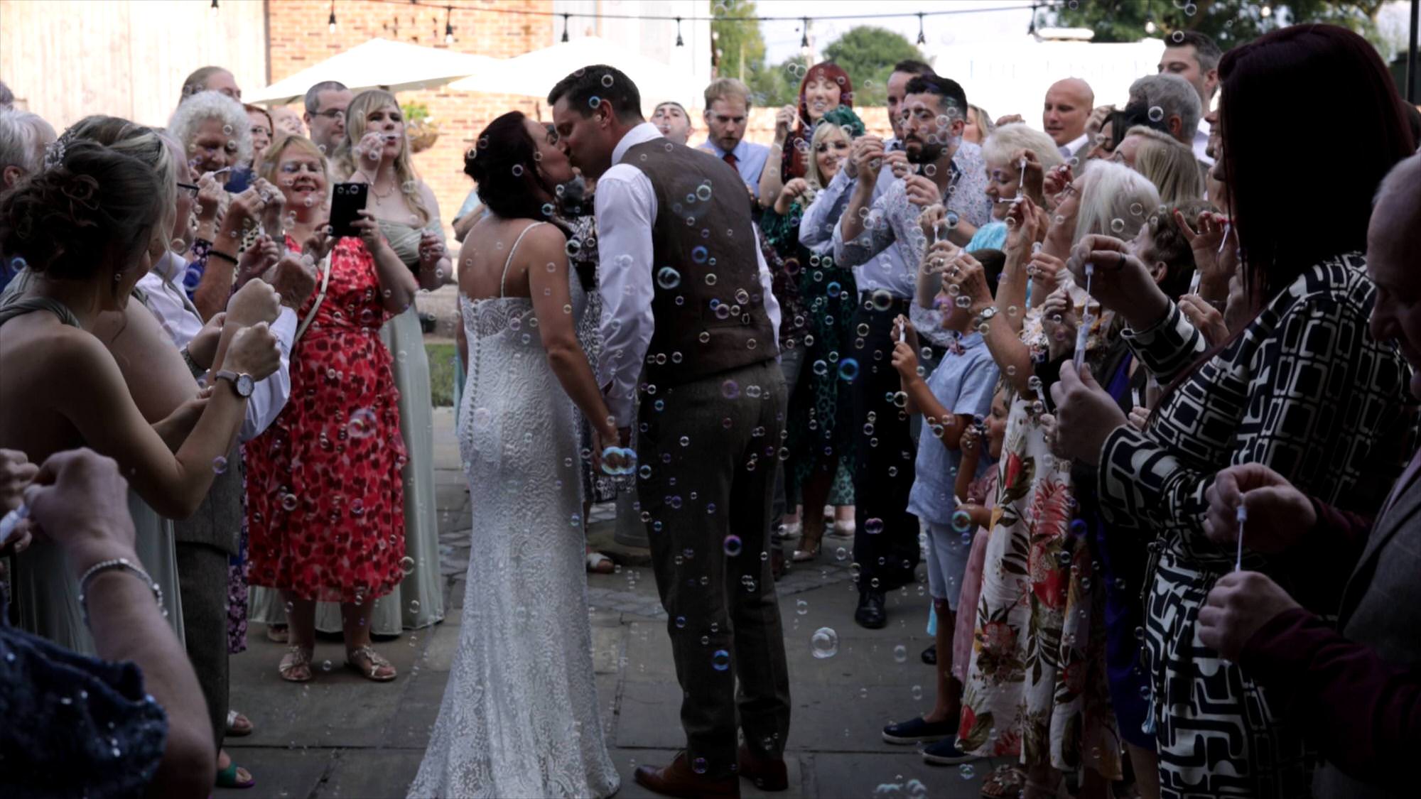 a couple kiss surrounded by guests blowing bubbles at their wedding reception