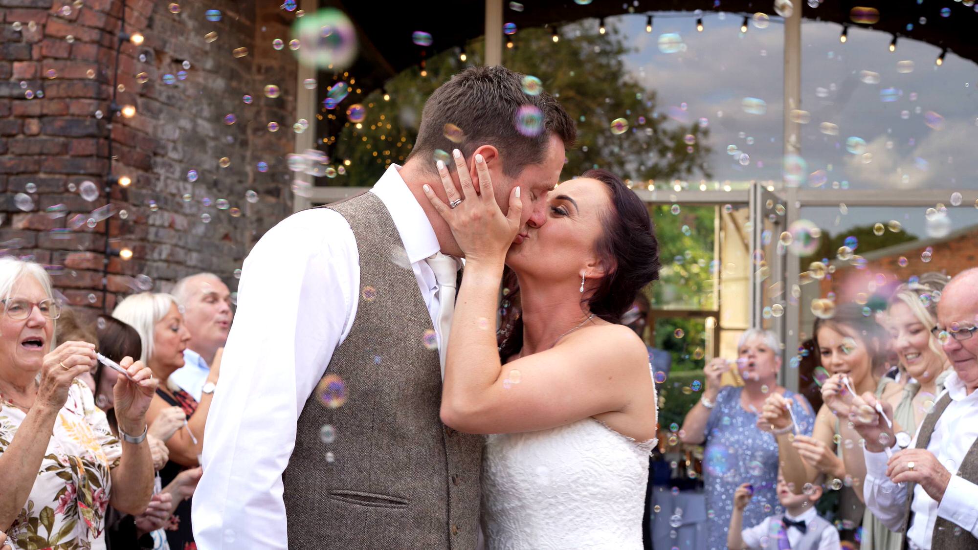 the couple kiss for the wedding videographer during bubbles at the barn at morleys hall