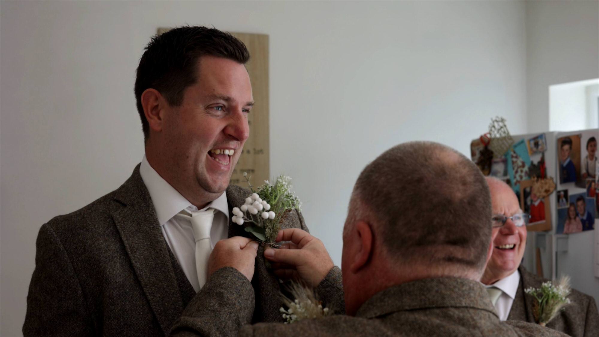 a groom laughs as he has his button hole pinned