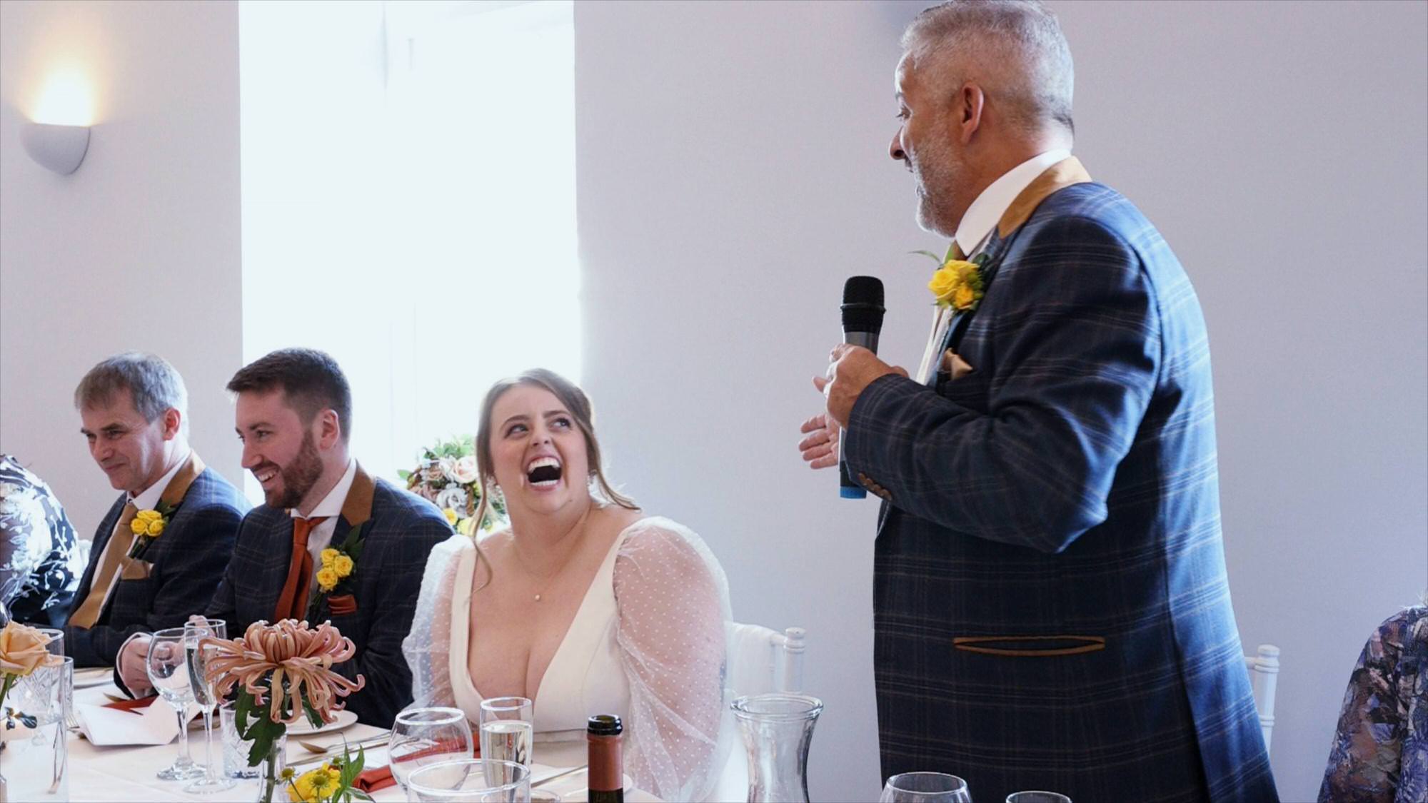 a bride laughs at her dad during his speech at Cartmel Old Grammar