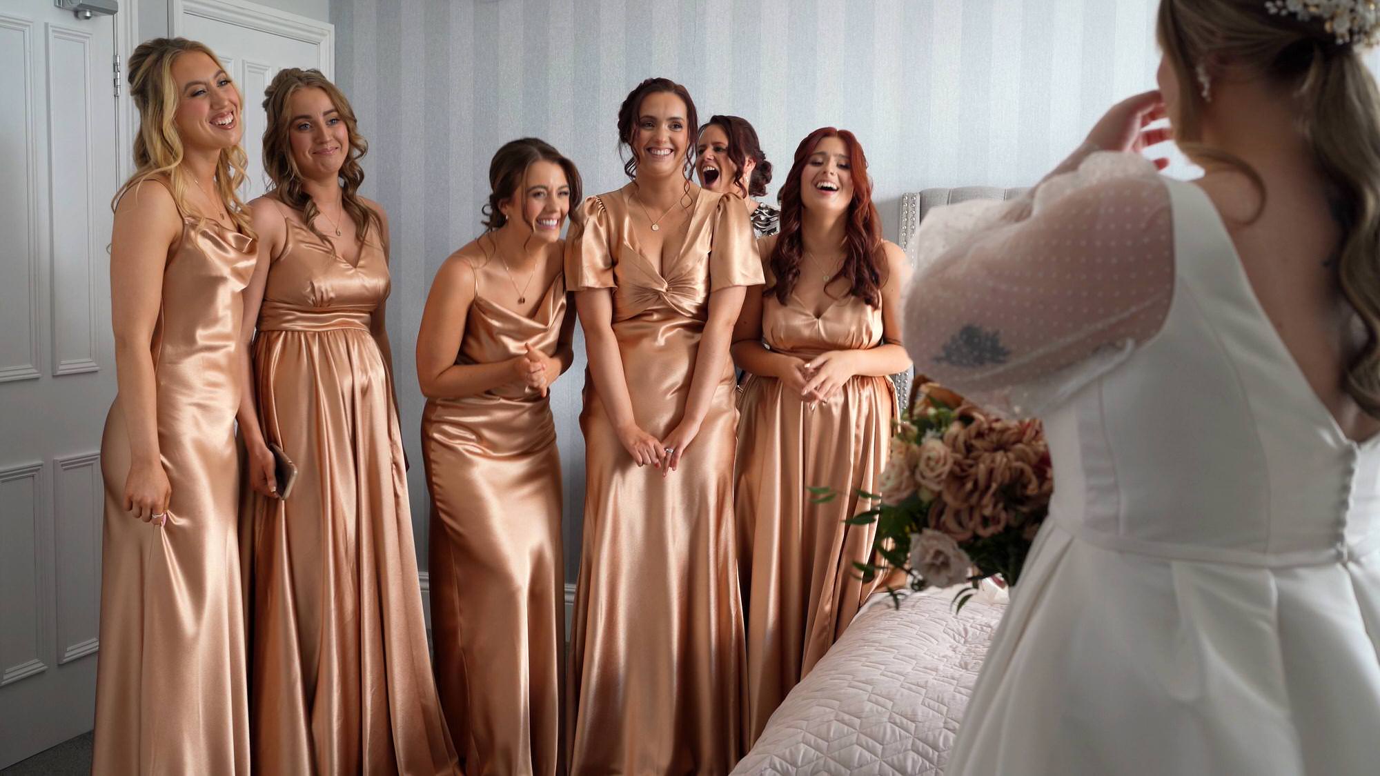 bridemaids wearing bronze satin dresses gasp at the brides first look