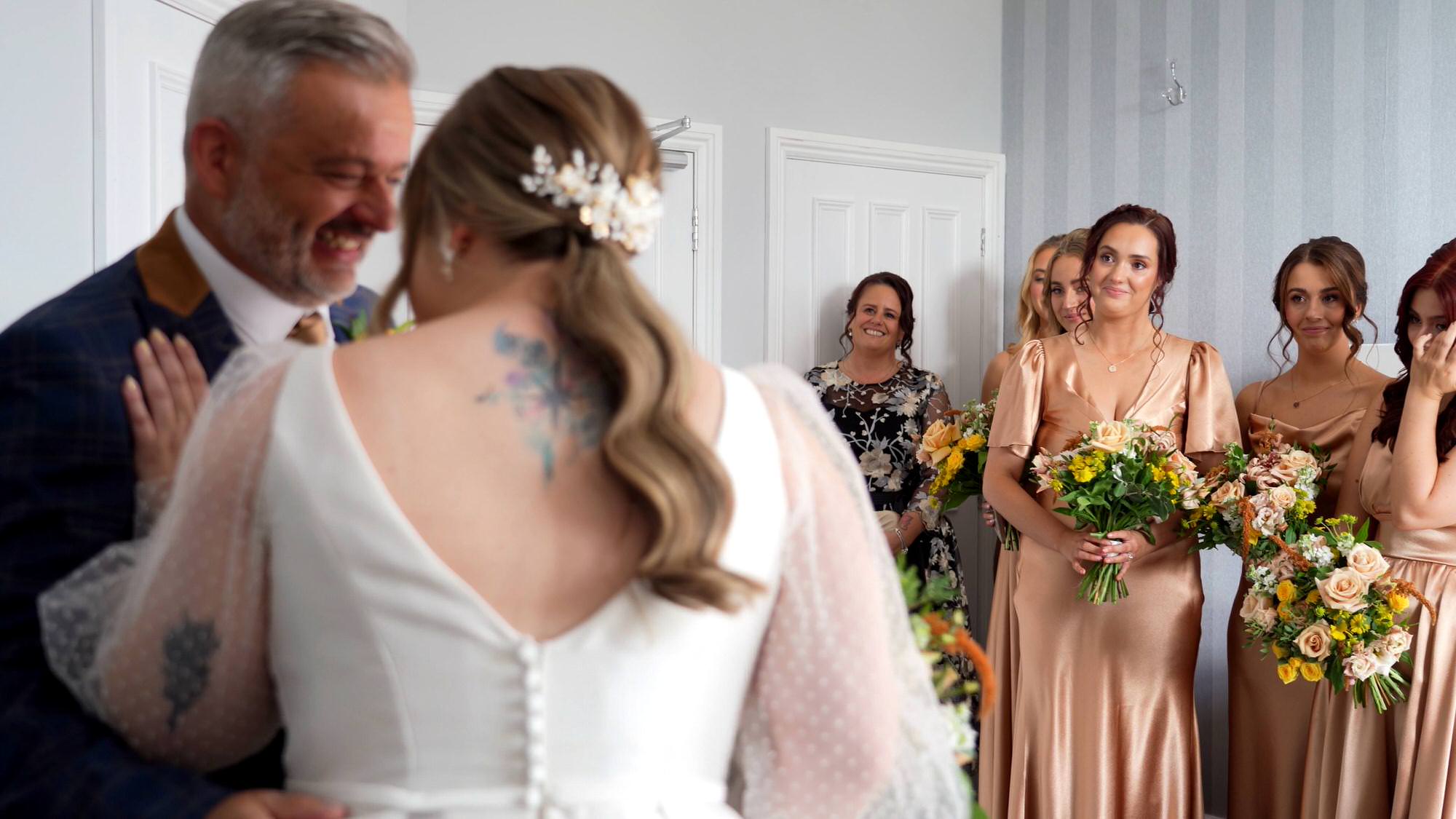 videographer films the bridesmaids wiping tears as the bride laughs with dad