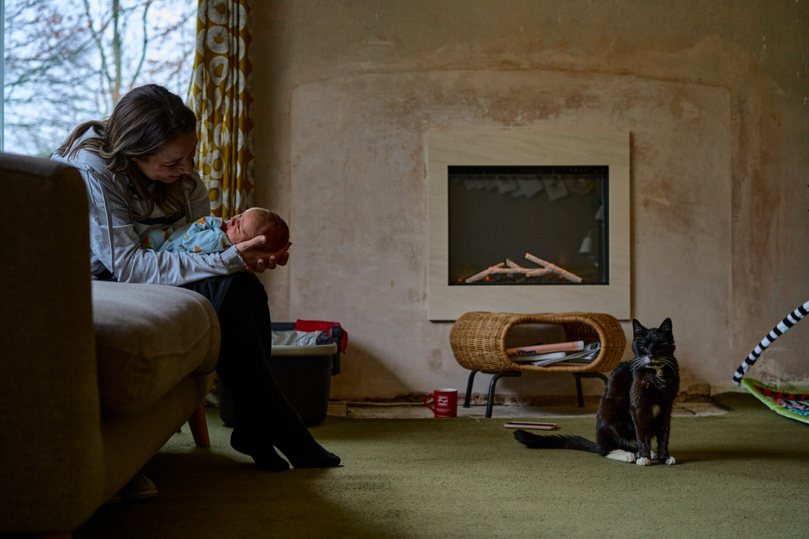 a mum smiles at her baby whilst their pet cat sits close-by during a candid photoshoot at home in Ormskirk