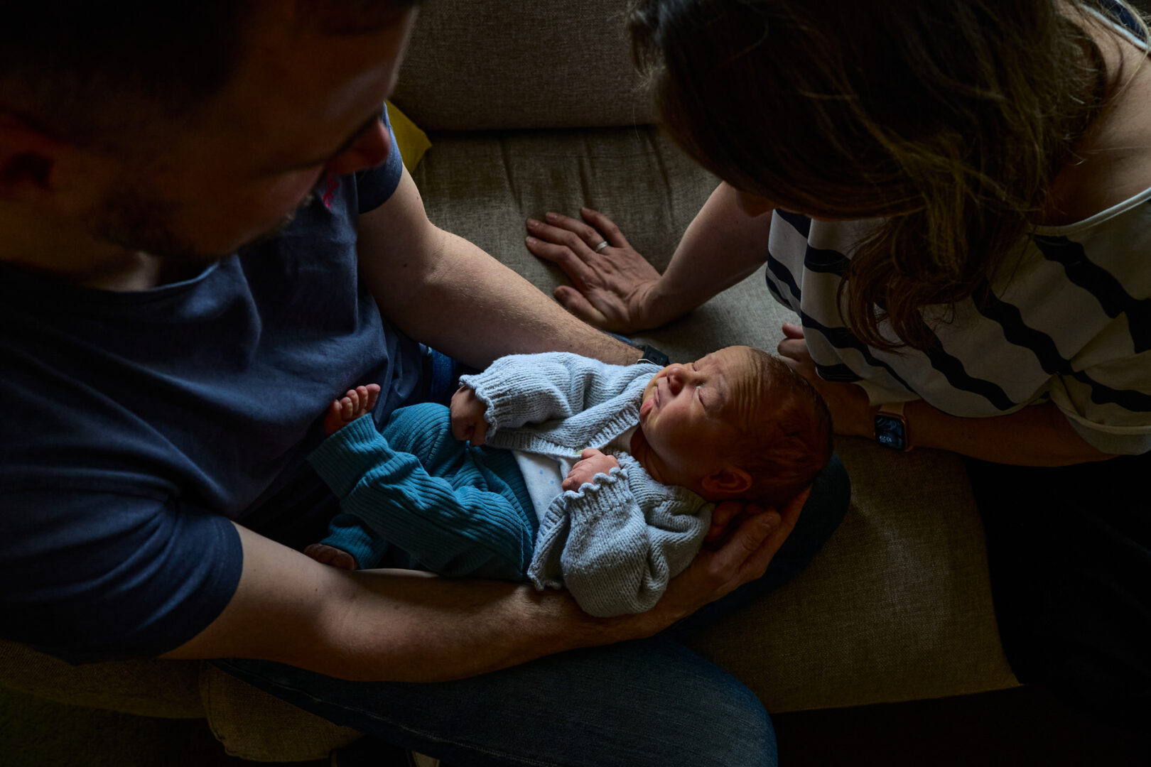 a natural photo of a mum and dad looking down at baby with some beautiful natural light at home