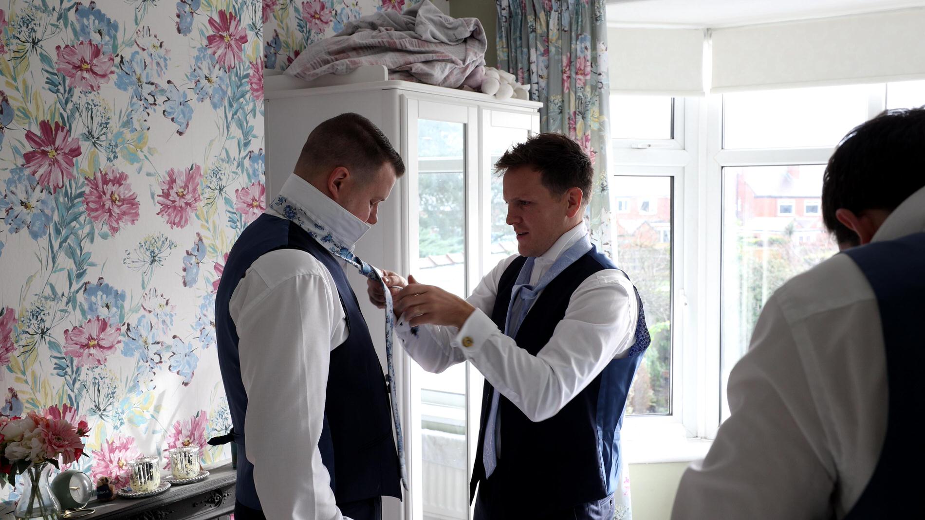 a groomsman helps the groom with his tie