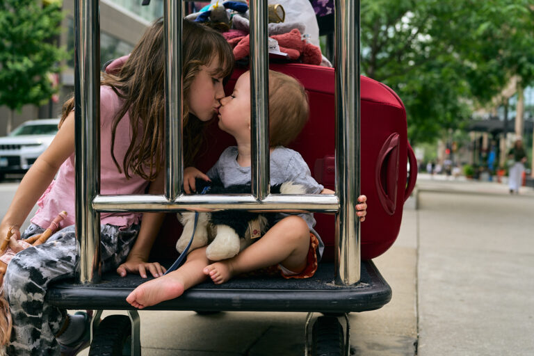 a photo of a child and toddler kissing sat next to holiday luggage to melt a parents heart