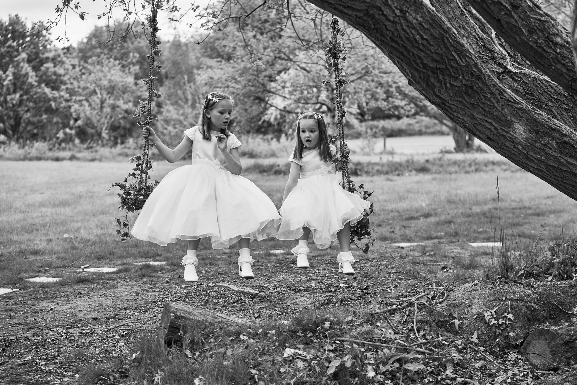 two girls in white christening dresses sit on a tree swing outside Holland Hall in Upholland
