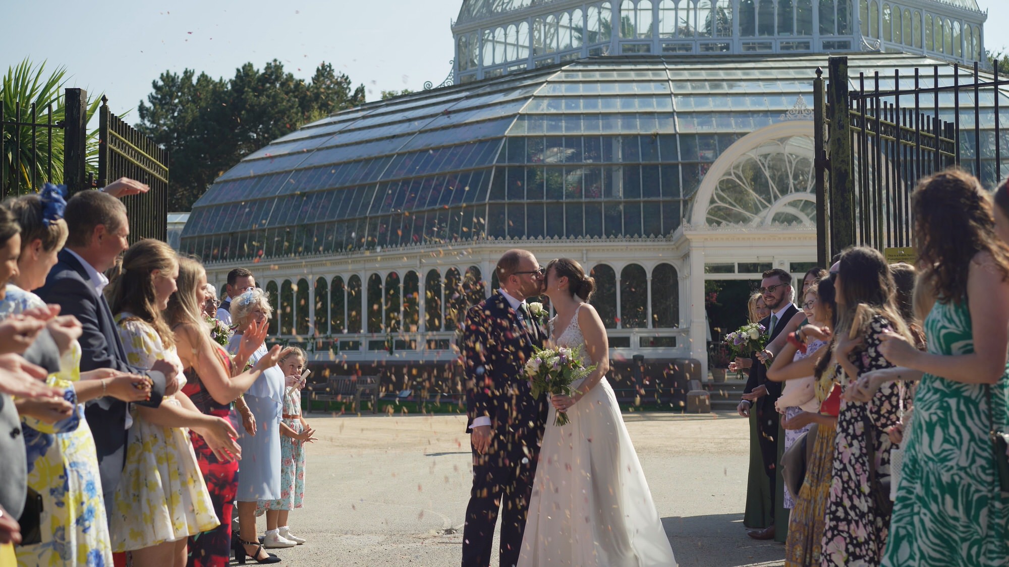 Kirsty and Josh Sefton Palm House Wedding Video 17 a couple kiss during petal confetti outside Sefton Park Palm House