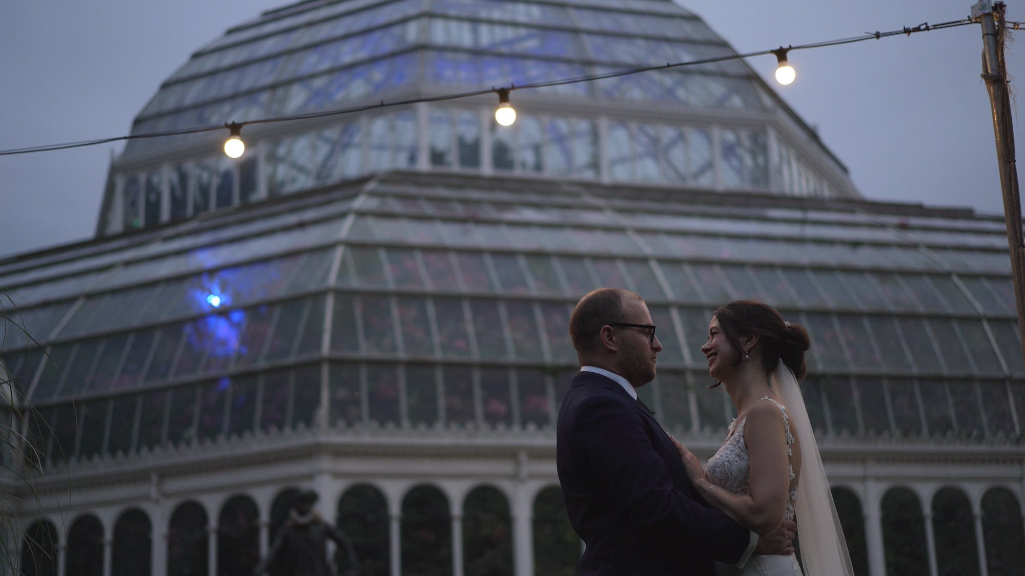 Kirsty and Josh Sefton Palm House Wedding Video 34 a video still of a couple at dusk under festoon lights at Sefton Park Palm House Liverpool