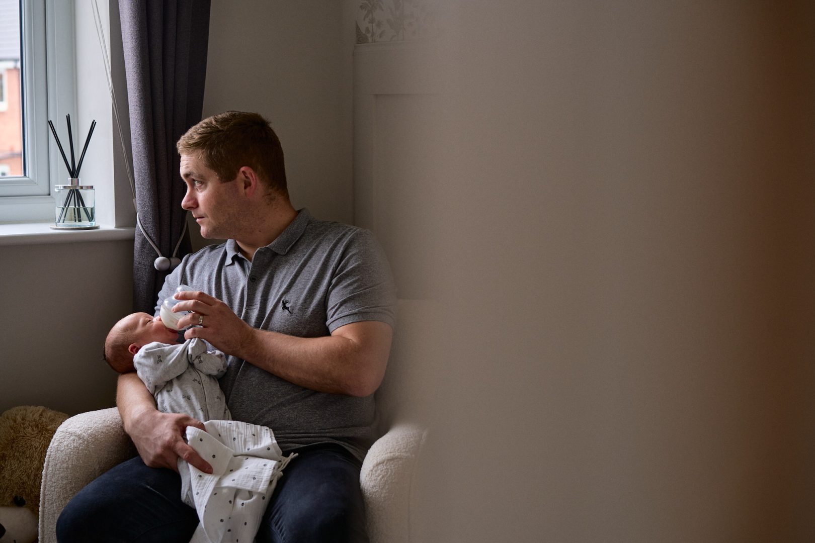 a documentary photo of a dad relaxing on the nursery chair feeding his newborn baby in Warrington