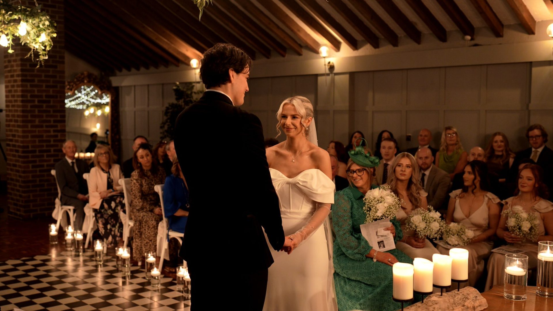 a couple smile at each other during a candlelit black tie wedding ceremony at Larkspur Lodge in Cheshire