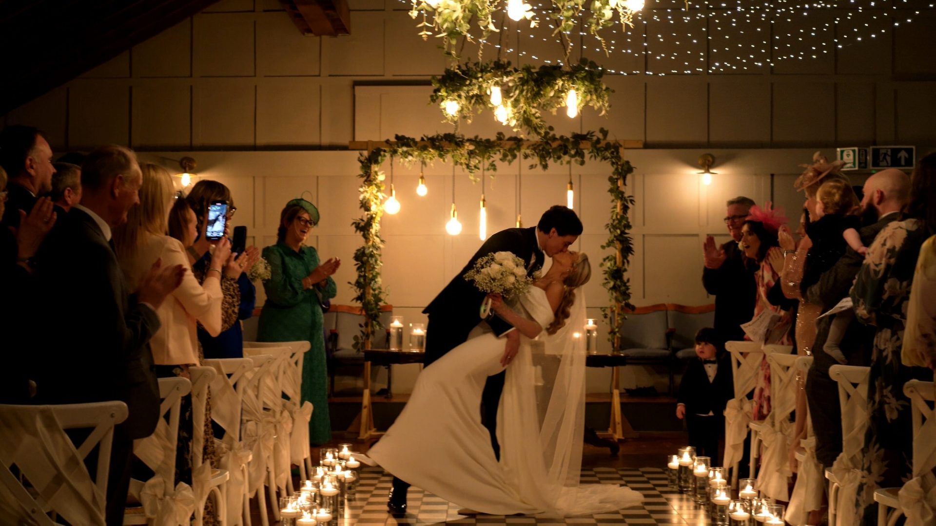 the couple dip for a kiss walking down the aisle at Larkspur Lodge in Knutsford