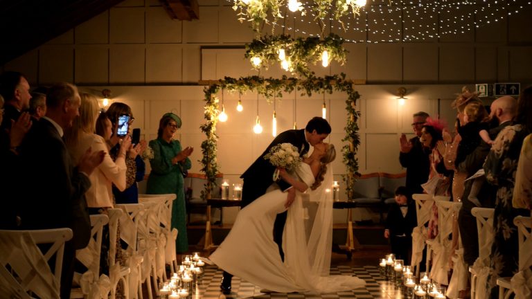 the couple dip for a kiss walking down the aisle at Larkspur Lodge in Knutsford