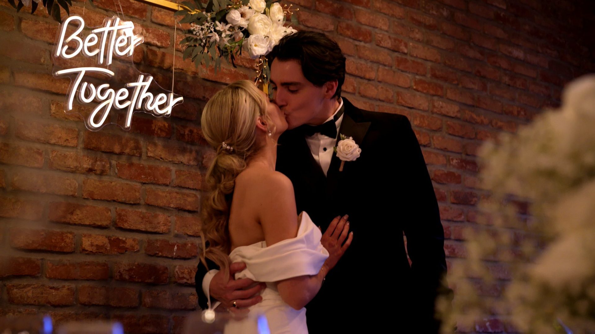 a couple kiss by a Better Together neon sign by an exposed wall at Larkspur Lodge in Cheshire