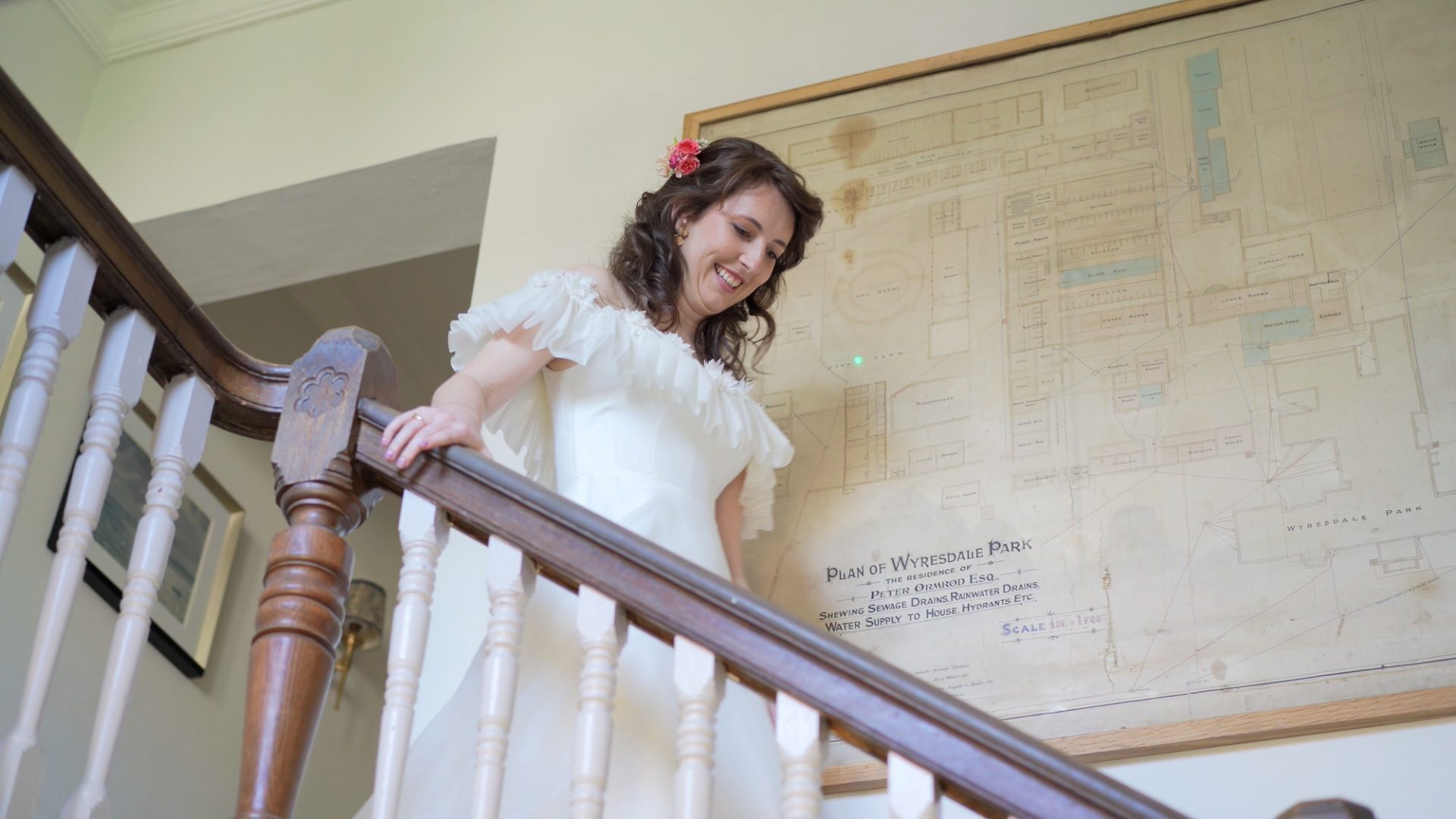 a bride wearing a vintage style dress with flowers in her hair walks down the stairs