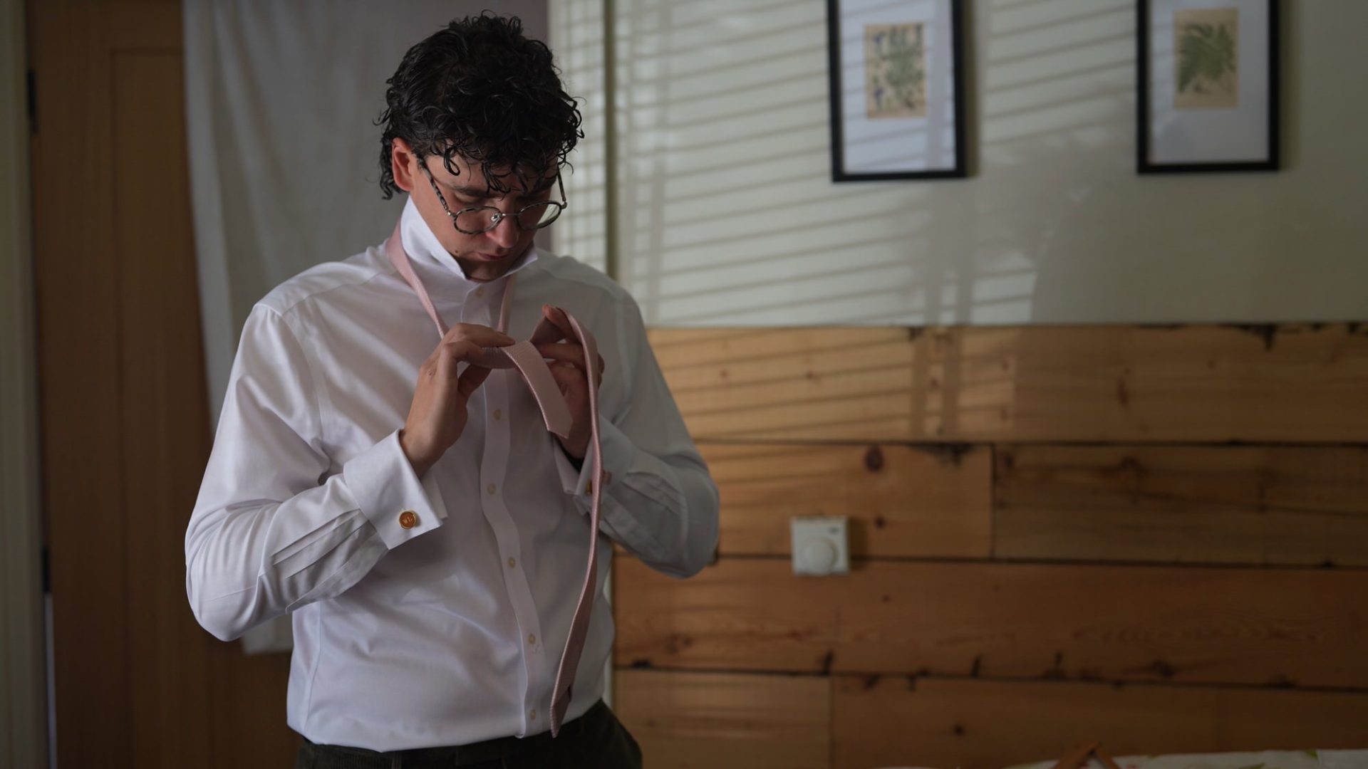 a groom ties his pale pink tie in the lodge at Wyresdale Park