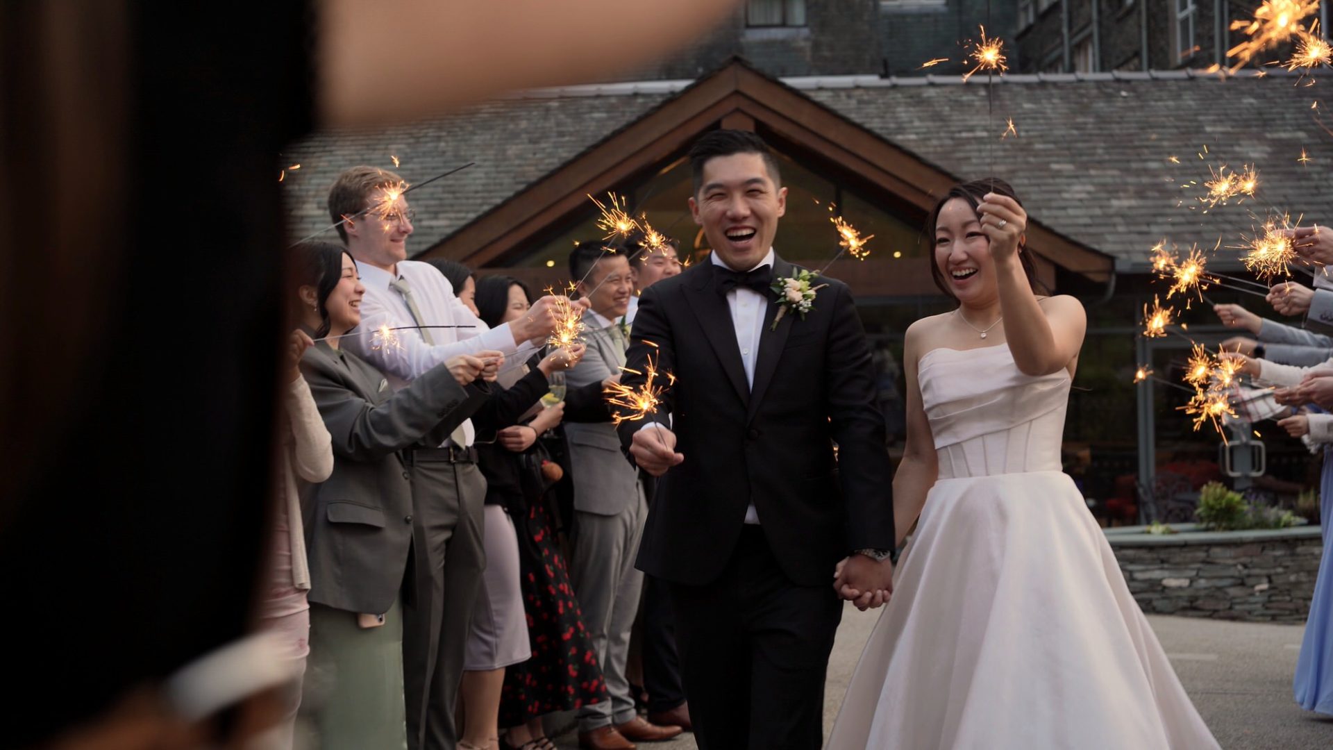 a couple laugh as they join guests with sparklers for their evening reception at Lodore Falls
