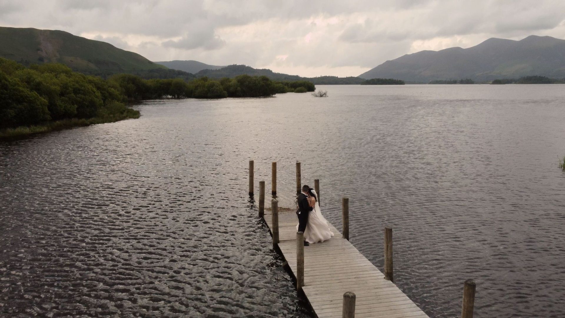 an aerial drone shot of a bride and groom on a jetty by Derwentwater near Lodore Falls