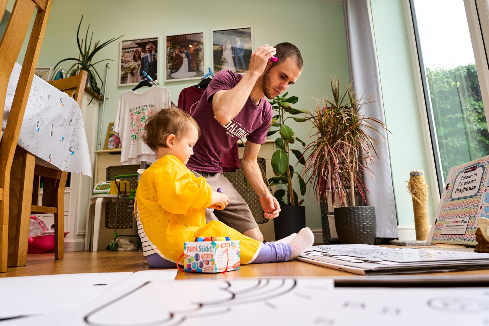 a dad adds a paint stick behind his ear as he prepares to build a hobbycraft house with his daughter