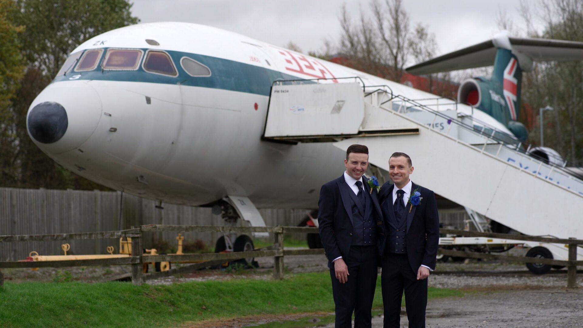two grooms pose by aircraft at Manchester Airport runway visitor park