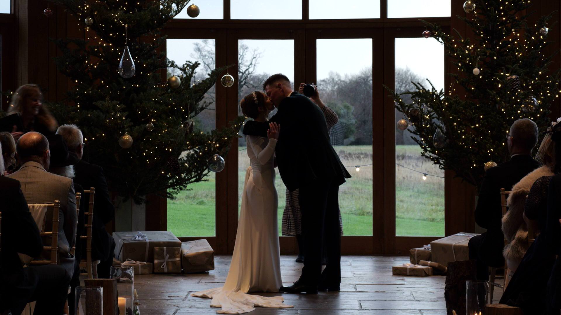 a first kiss by the Christmas trees at a wedding ceremony at the Out Barn