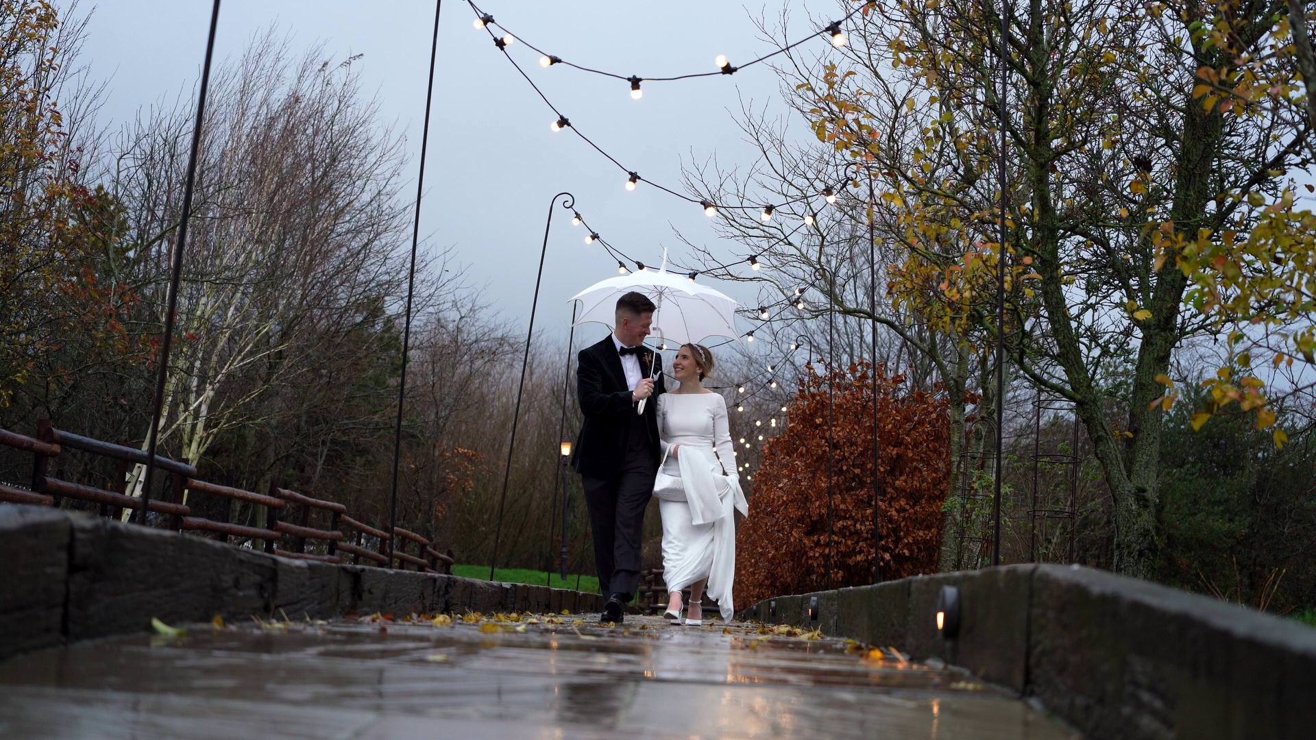 A couple walk along in the rain during a winter wedding at the Out Barn