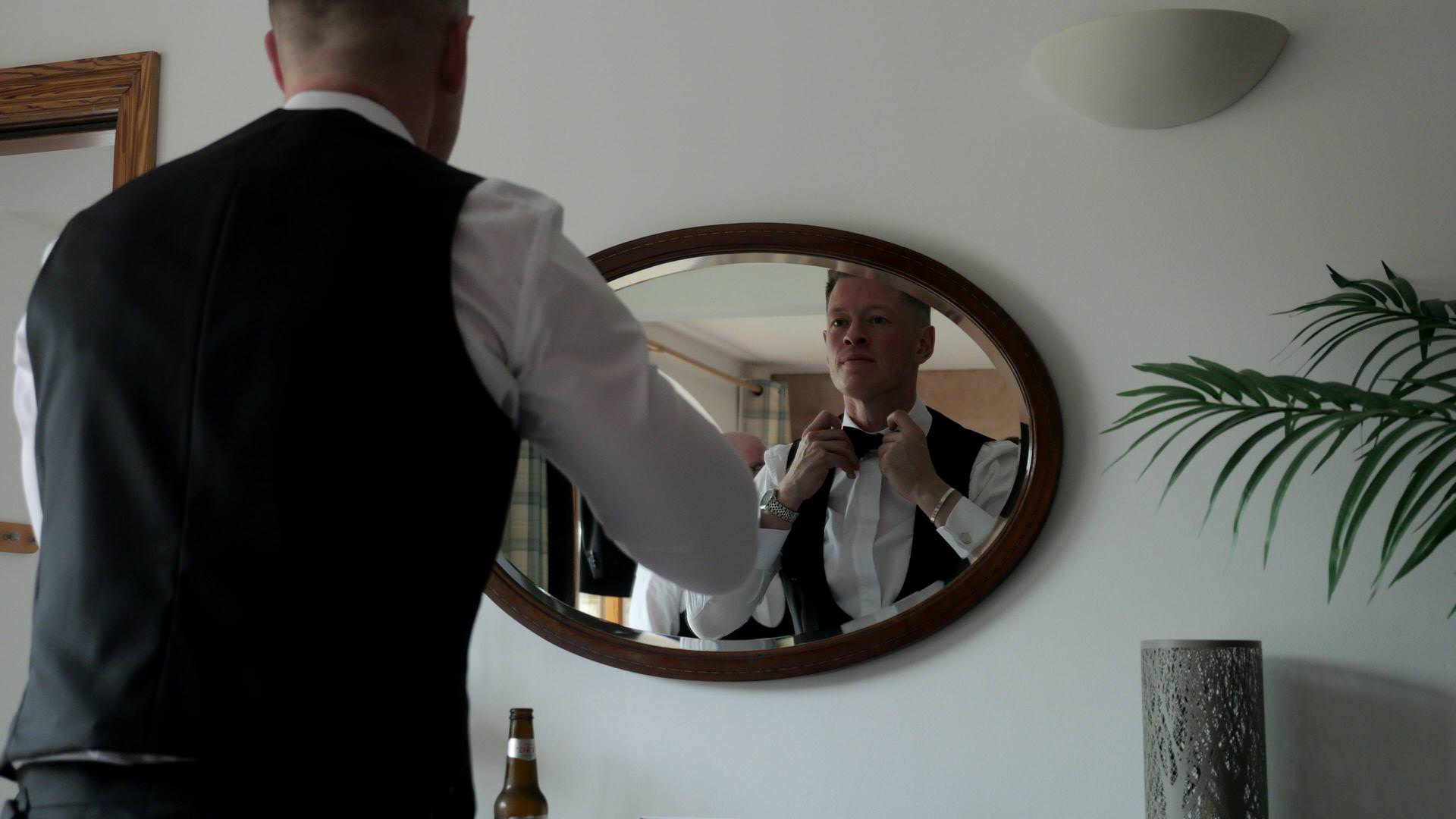 a groom fixes his bow tie at the luxury lodge cottage at the Out Barn