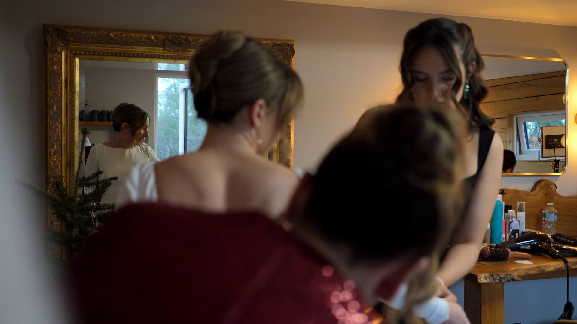 mum and maid of honour help the bride into her wedding dress in the dressing room