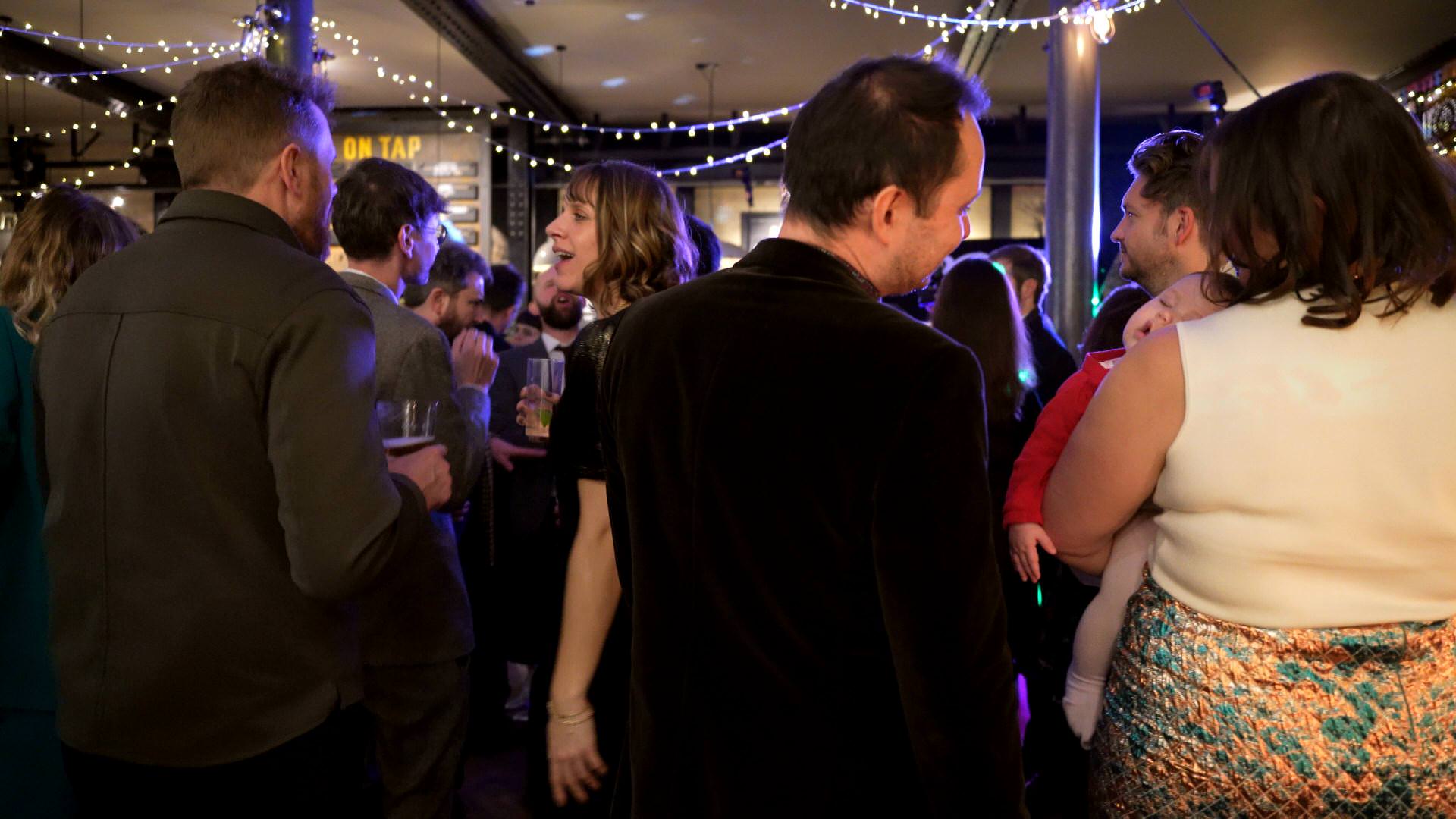 a baby sleeps on a mums shoulder as the party continues