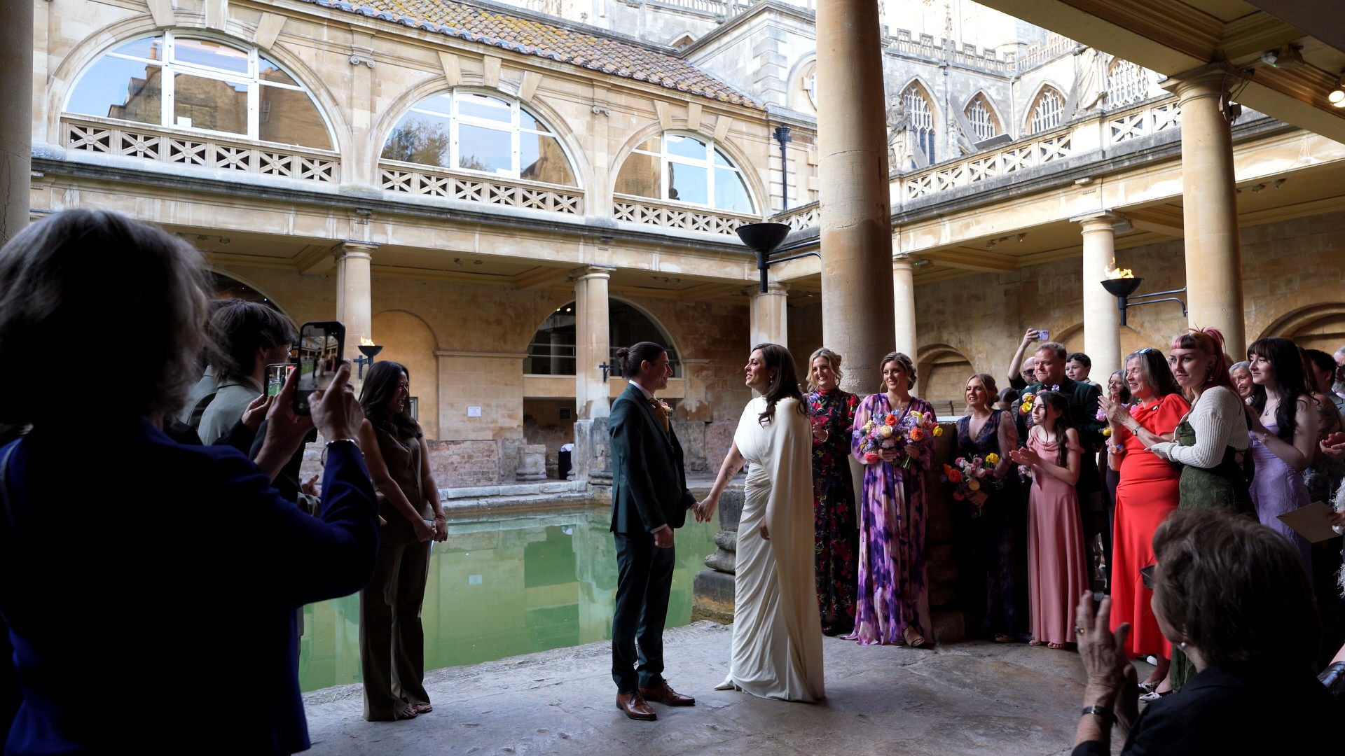 couple stand together by the baths as guests cheer