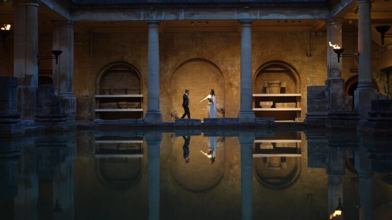 a stunning evening shot of a couple walking around torch lit Roman Baths after vow renewal