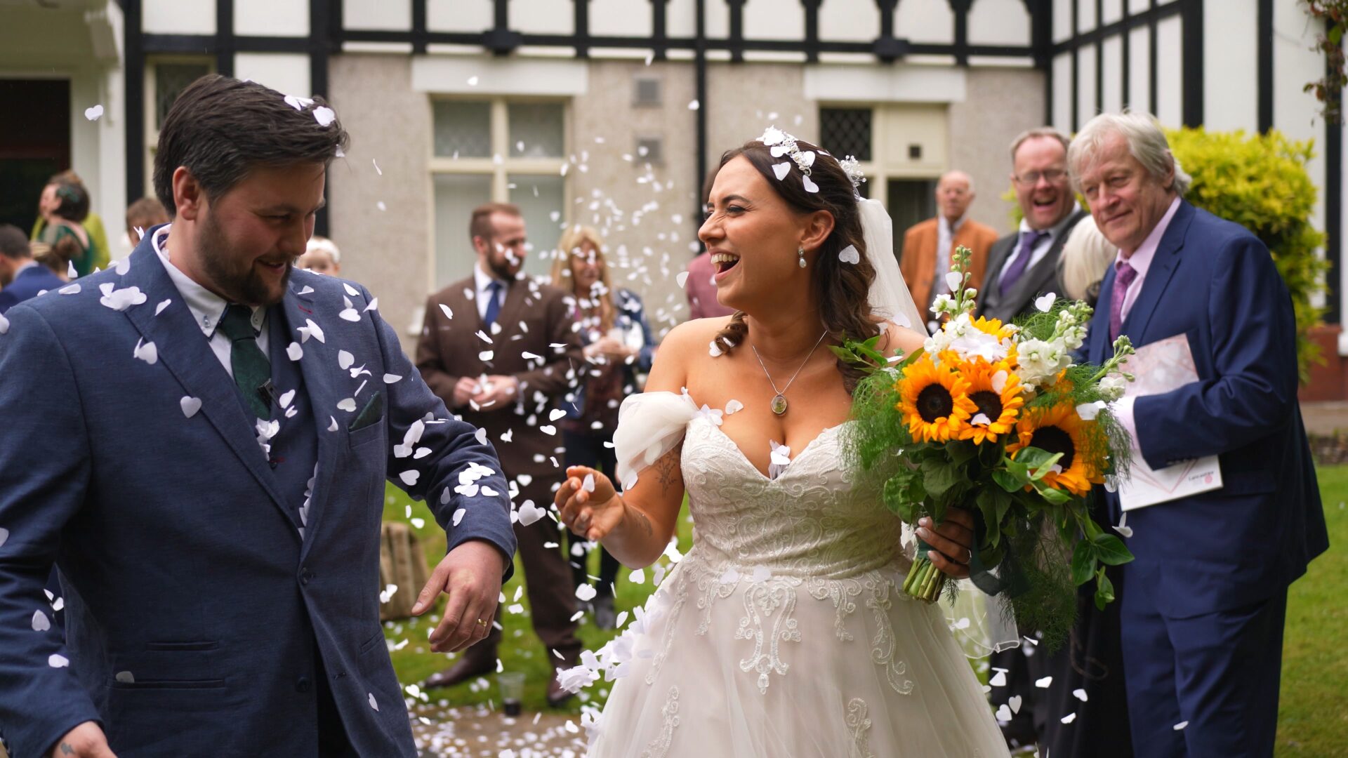 the couple laugh as they walk through confetti thrown in the rain outside Wyre Civic Centre