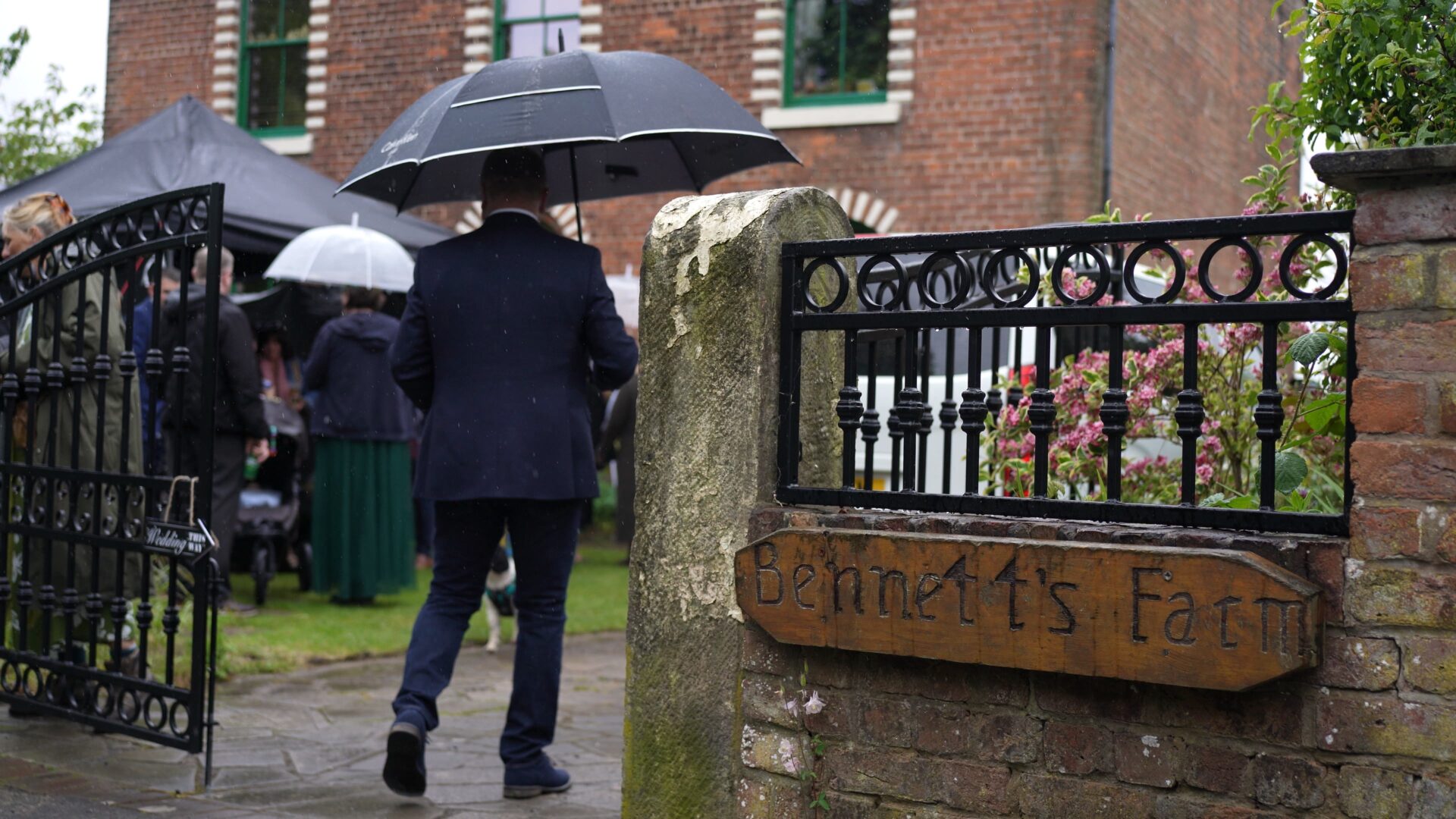 Guests walk into the family farmhouse gate with umbrellas
