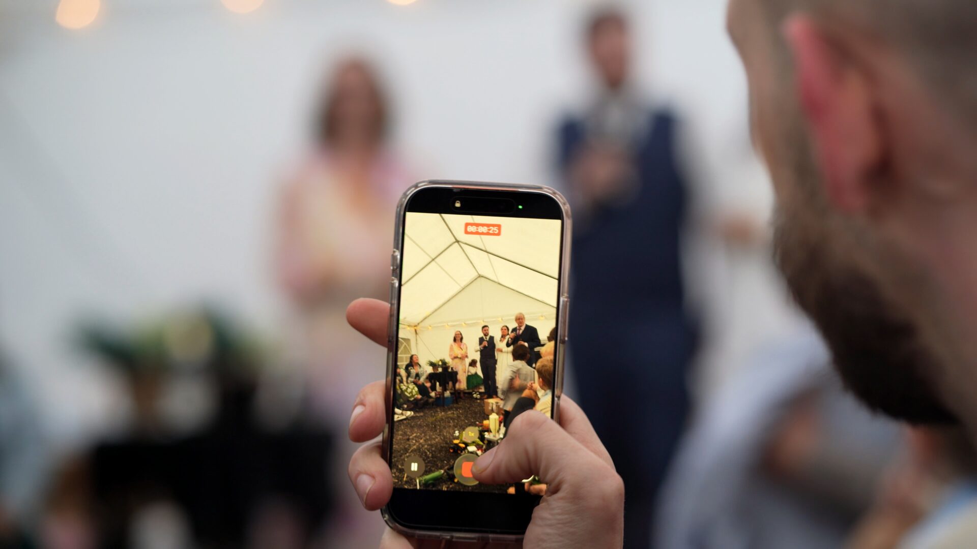 a unique candid video still of the wedding speeches being filmed on a phone