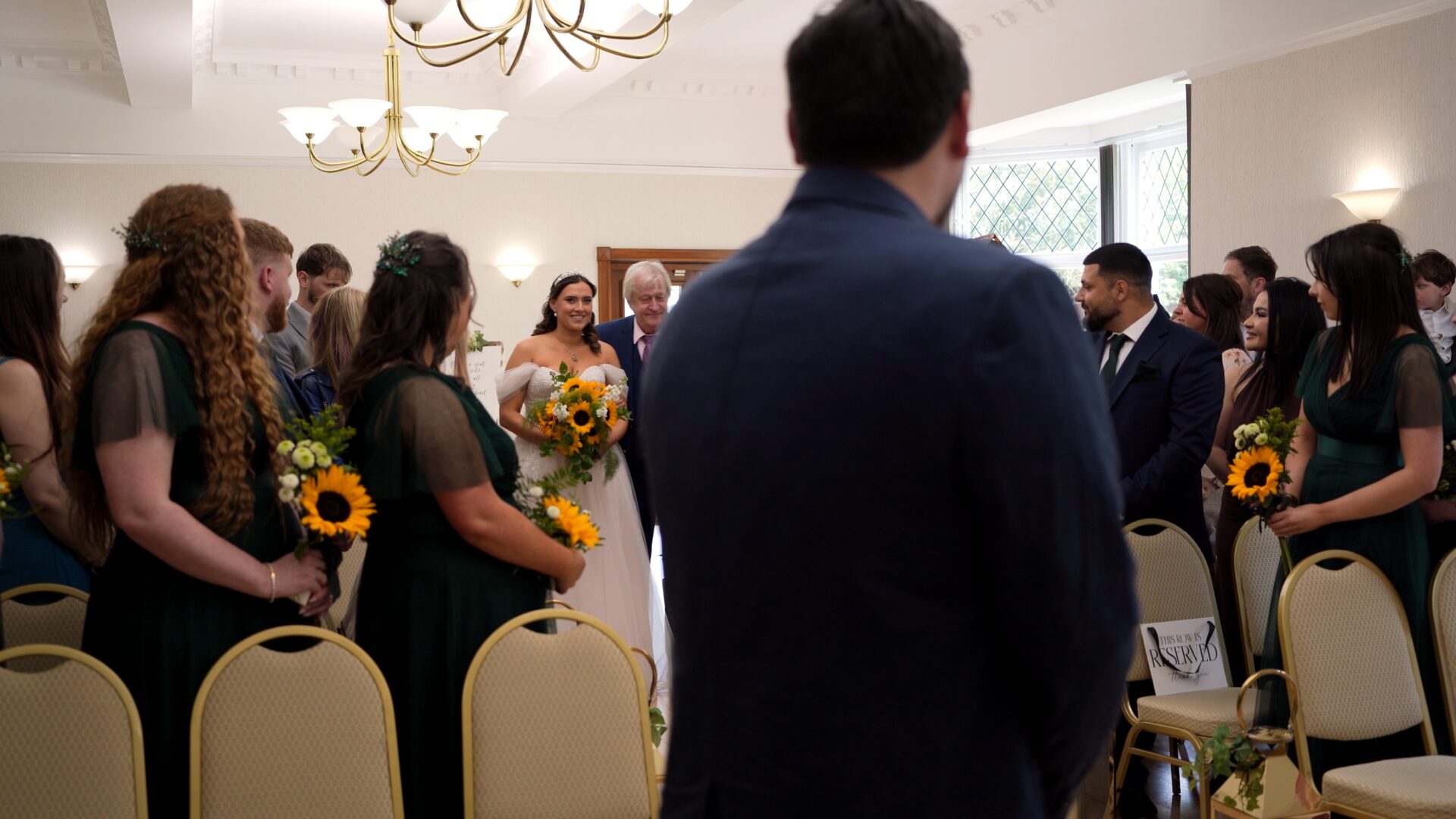 a bride carrying a bouquet of sunflowers walks down the aisle at the Wyre Civic Centre