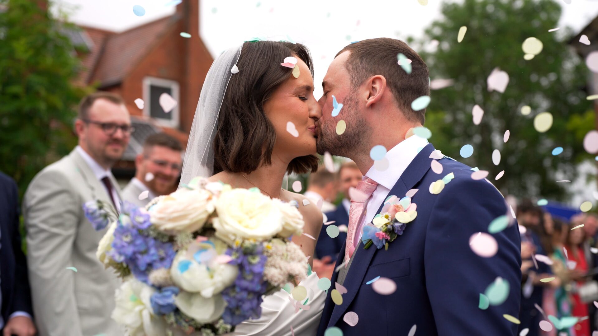 a candid wedding videographer captures a kiss outside the church during their confetti run in the rain in Harrogate